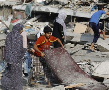Menino palestino carrega colchão retirado dos escombros do apartamento de sua família, bombardeado nesta terça-feira (22) no centro da cidade de Gaza 