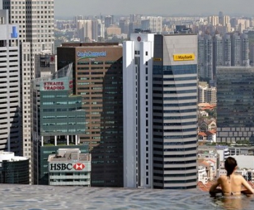 Hóspedes do hotel Marina Bay Sands, em Cingapura, observam a cidade de uma piscina com lateral que termina em queda d'água, no topo do edifício. 