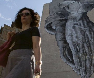 Mulher passa por prédio com arte de mãos em oração em Atenas, Grécia, nesta quinta-feira (25) 