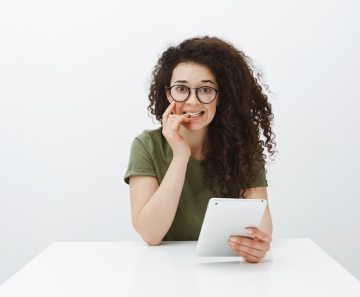 worried_insecure_good_looking_female_student_with_curly_hair_sitting_table_with_digital_tablet