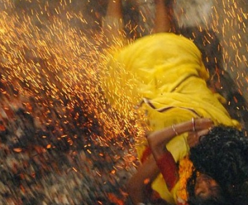 Devota hindu cai em carvão quente enquanto segura a filha durante uma corrida sobre carvão na Índia 