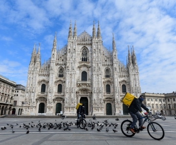 Ciclistas que trabalham com entrega de alimentos passam pela Piazza Duomo em Milão, na Itália, que estava deserta na terça-feira (31) — Foto: Piero Cruciatti / AFP