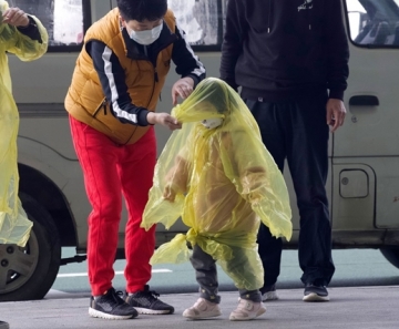Mulher com máscara improvisa cobertura para proteger crianças de contaminação pelo novo coronavírus em aeroporto de Wuhan, na China, nesta quarta-feira (8) — Foto: Han Han Guan/AP